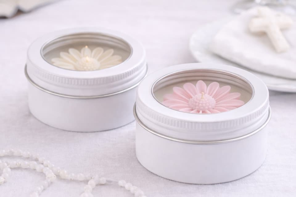 Bougies en boîtes métalliques blanches, avec motif floral moulé rose et blanc, présentées comme attention finale ou remerciement lors d’un événement