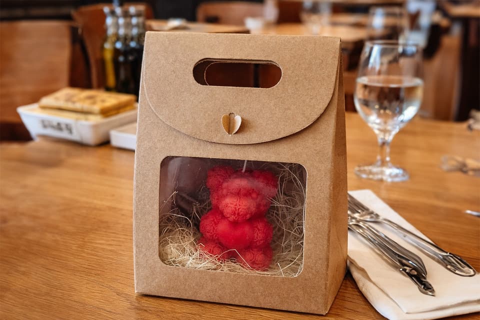 Bougie moulée rouge en forme d’ours présentée dans un coffret cadeau en kraft sur une table dressée