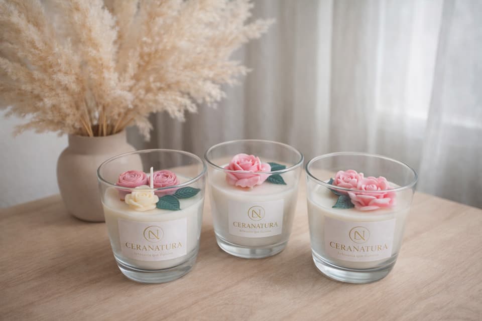Bougies Ceranatura en verre décorées de fleurs moulées roses et crème, posées sur une table en bois clair