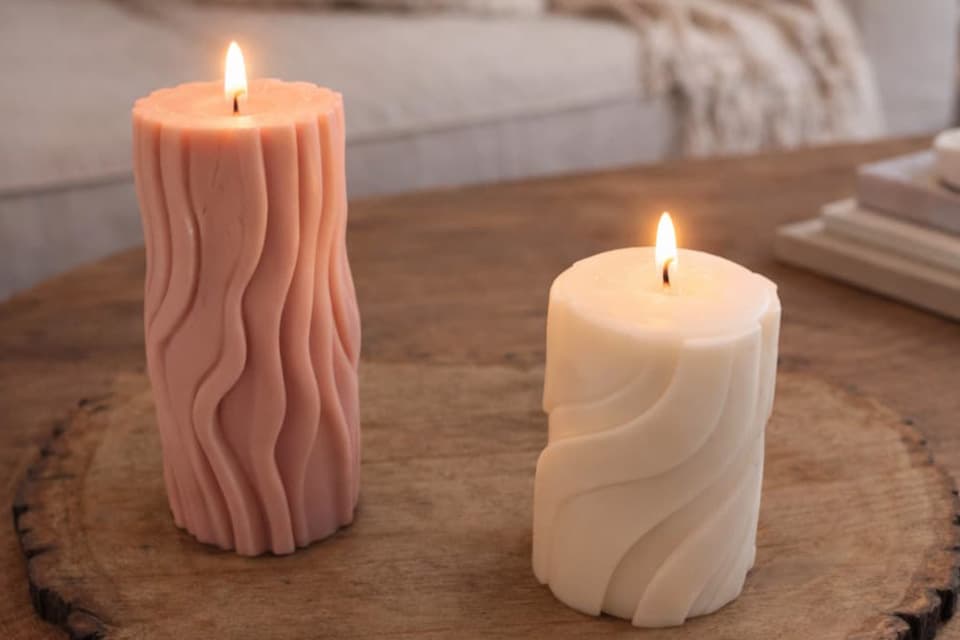 Bougies moulées allumées, rose et blanche, avec relief ondulé, posées sur une table en bois