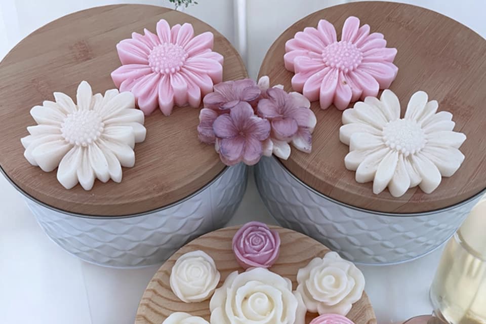 Bougies moulées en forme de fleurs, en teintes pastel, présentées sur des couvercles en bois et un plateau